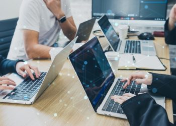 4人の人がひとつの机でそれぞれ自分のノートパソコンを開いて使っている様子